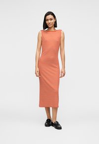 Midi φόρεμα με ρίγες σε πορτοκαλί και λευκό, με εφαρμοστή σιλουέτα, χωρίς μανίκια και με ευθεία λαιμόκοψη. Φορεμένο με μαύρα παπούτσια.