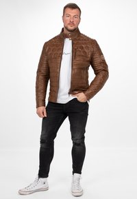 Bruine leren bomberjack met een honingraattextuur, ritsluiting en een staande kraag. Gecombineerd met een witte t-shirt en zwarte skinny jeans.