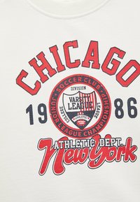 Witte sweatshirt met opvallende rode en blauwe grafische afbeeldingen. De tekst bevat "CHICAGO," "1986," en "New York" met een varsity schildontwerp.