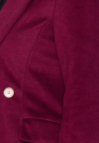 Bordeauxroter Blazer aus strukturiertem Stoff, mit Ein-Knopf-Verschluss und strukturierten Schultern. Auffällige Nahtdetails und Tasche.