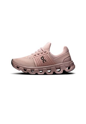 Chaussure de sport rose clair avec une semelle amortissante comportant des segments creusés et un logo noir sur le côté, visible de profil sur fond blanc.