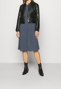 Svart läder kort jacka, blå klänning med vitt hjärt-mönster, ankelstövlar; slät textur, skräddarsydd passform och lagerdesign.