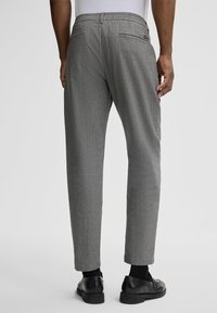 Gray, textured dress pants with a slim fit, featuring back pockets and a waistband, paired with black dress shoes.