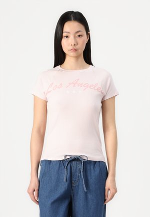 Light pink cotton t-shirt with "Los Angeles" in cursive, short sleeves, and a round neckline. Paired with casual denim trousers.
