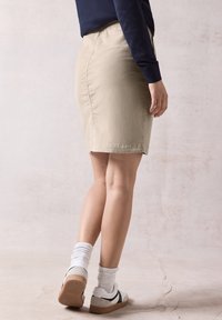 Beige sukně po kolena vyrobená z bavlny, s hladkou texturou a elastickým pasem. Nosená s bílými ponožkami a sportovními teniskami.