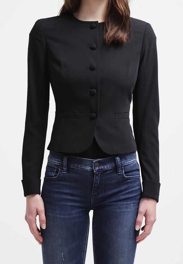 Svart skräddarsydd jacka med rund krage, sex framknappar och långa ärmar. Kombinerad med mörkblå jeans ser tyget slätt och strukturerat ut.