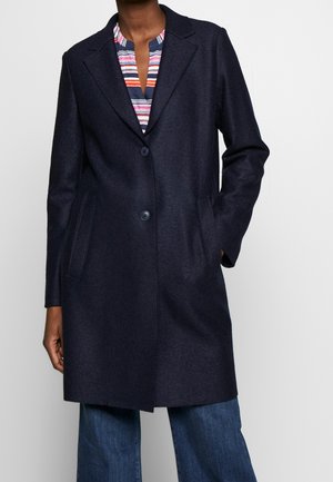 Dark navy blue wool coat with two buttons, notch lapels, and welt pockets worn over a colorful striped blouse and blue jeans.