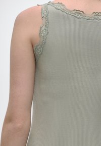 Κοντινή λήψη της πλάτης ενός ατόμου που φοράει ένα ριμπ, ανοιχτό πράσινο τοπ με δαντέλα κατά μήκος των ιμάντων των ώμων.