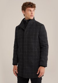 Svart och grå rutmönstrad kappa med hög krage, texturerad tyg, framfickor och en strömlinjeformad siluett, bärs över en svart dragkedjetröja.