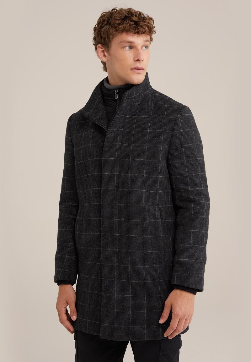 Svart och grå rutmönstrad kappa med hög krage, texturerad tyg, framfickor och en strömlinjeformad siluett, bärs över en svart dragkedjetröja.