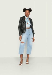 Jaqueta de motociclista de couro preto, top halter azul claro com recorte em forma de olho-chave, jeans cropped de lavagem clara e desgastada, e sandálias brancas de salto.
