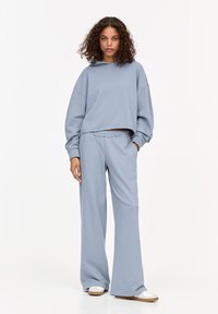 Un hoodie court bleu clair avec des manches larges, associé à un pantalon ample assorti. Le tissu semble doux avec une texture lisse.