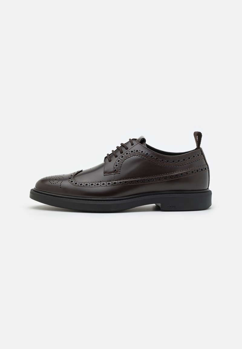 Chaussure brogue en cuir marron foncé avec motifs perforés, lacets à l'avant et semelle noire sur fond blanc.