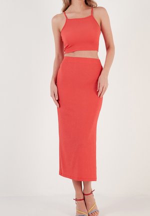 Femme portant une tenue corail ajustée composée d'un crop top et d'une jupe midi taille haute, assortie à des talons multicolores à lanières.