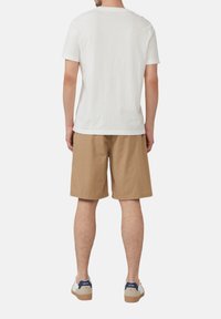 Weißes kurzärmliges T-Shirt, lockere Passform, kombiniert mit hellbraunen Shorts mit einem strukturierten Muster. Legere Sneaker mit blauen Akzenten.