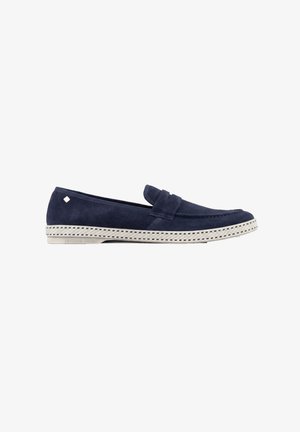 Marineblauwe suède loafer met witte rubberen zool met een geweven patroon en een klein rechthoekig metalen detail vlak bij de hiel.