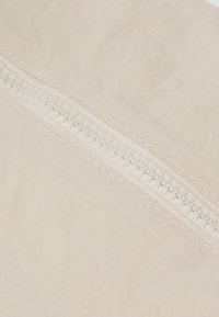 Tessuto beige con una cerniera bianca visibile, un design testurizzato, bordi cuciti e una superficie liscia.