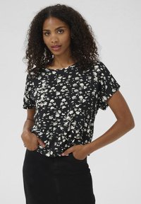 Black short-sleeve blouse with an abstract white floral pattern, featuring a round neckline and relaxed fit, worn with a black skirt.