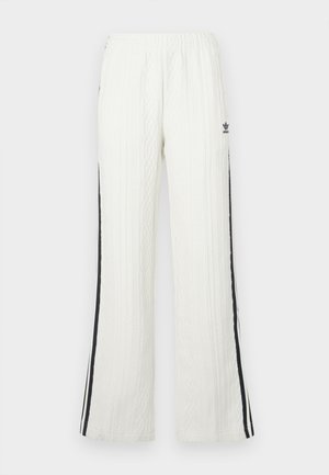 Baltas teksturēts Adidas bikses ar melnām svītrām sānos un mazu logotipu augšējā kreisajā augšstilbā, elastīga josta un taisnas kājas.