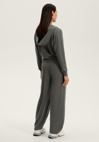 Hanorac gri cu glugă, cu o croială lejeră, asociat cu pantaloni gri cu picioare largi. Textură moale, detaliu minim și un design casual.