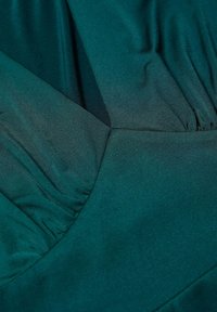 Gros plan sur un tissu en satin vert foncé avec des coutures froncées et pinces créant des textures lisses et froncées.