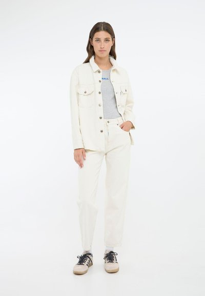 Chaqueta de denin blanca con dos bolsillos en el pecho, combinada con una camiseta gris y pantalones blancos. Unos zapatos deportivos negros y beige completan el conjunto.