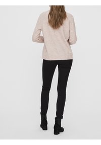 Pull rose clair à texture douce, associé à un jean skinny noir et des bottines à talons noires. Accent sur la simplicité et le confort.