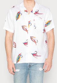 Biała koszula z krótkim rękawem z kolorowymi wzorami ryb, lekka tkanina, klasyczny kołnierzyk i kieszeń z przodu. Noszona z dżinsami typu distressed.