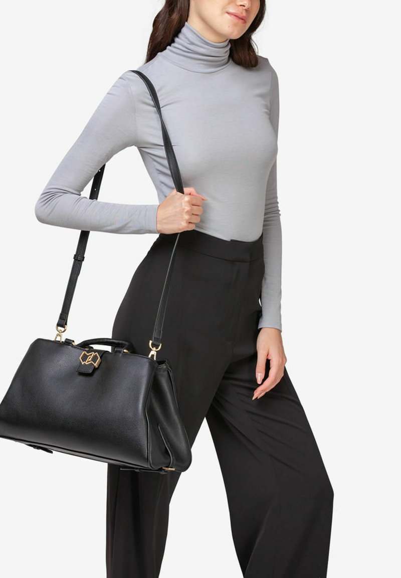 Sort læderhåndtaske med en struktureret form, gyldne hardware-detaljer og en aftagelig skulderrem, holdt af en person i en grå turtleneck.