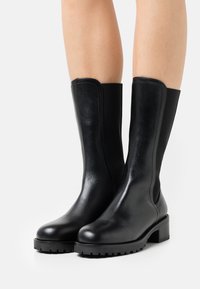 Botines negros de cuero con suela plana, paneles laterales elásticos y tacón cuadrado. Acabado liso con un mínimo de detalles de costura.