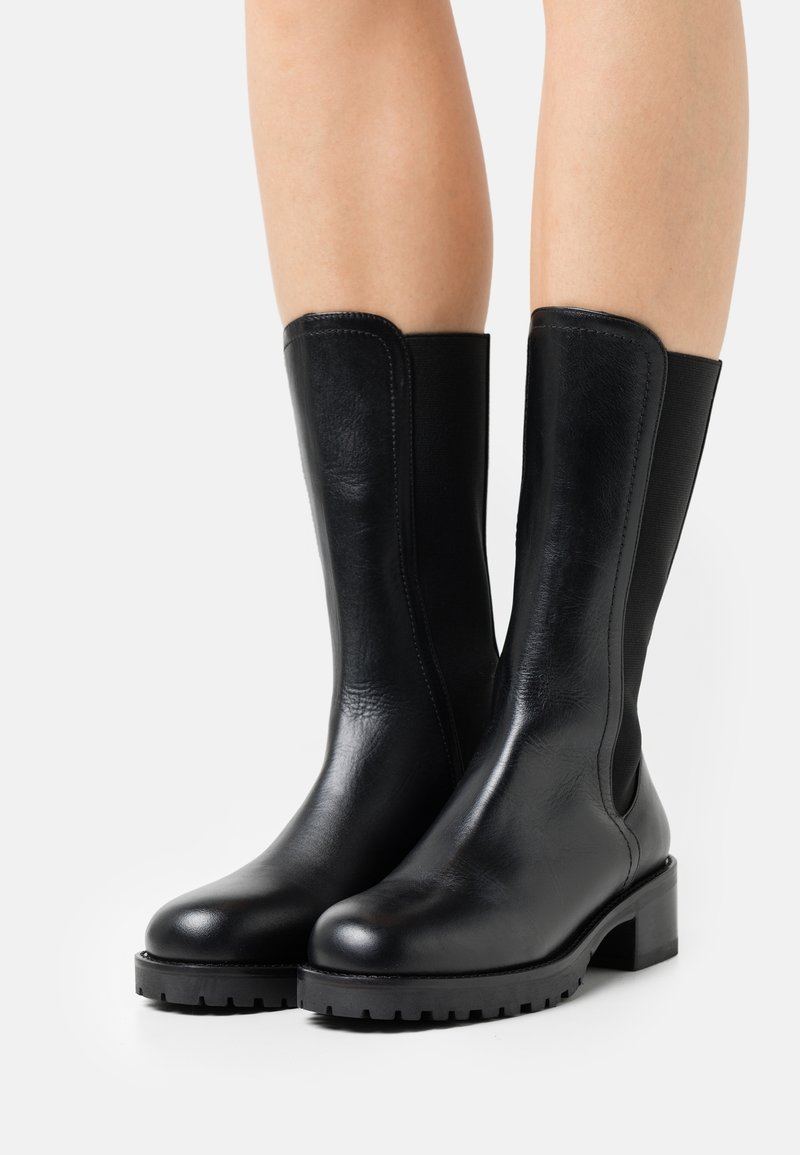 Botines negros de cuero con suela plana, paneles laterales elásticos y tacón cuadrado. Acabado liso con un mínimo de detalles de costura.