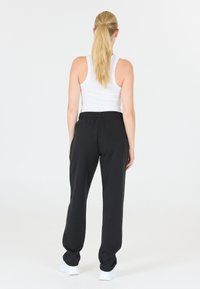 Svarta sweatpants med elastisk midja, lös passform och sidofickor, kombinerat med en vit linne och vita sneakers.