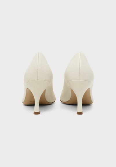 Paire de chaussures à talons hauts en cuir blanc vues de dos avec talons pointus et coutures visibles au centre.