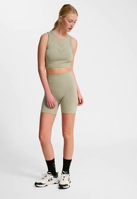 Ljusgrönt sportset med en figursydd croptopp och matchande högmidjade shorts, tillverkade av stretchigt material. Inkluderar vita sneakers och svarta strumpor.