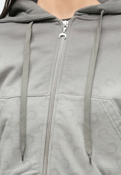 Φωτεινό γκρι φούτερ με υφή υφάσματος, διαθέτει ολόκληρο φερμουάρ, δύο εμπρόσθιες τσέπες και κορδόνια. Διακριτικό μοτίβο στο υλικό.