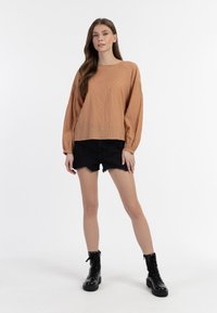 Rdzawoczerwony, teksturowany longsleeve z marszczonymi rękawami, połączony z czarnymi szortami dżinsowymi i czarnymi butami na sznurowadła. Prosty, casualowy wygląd.