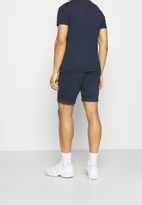 Mörkblå bomulls-t-shirt med kort ärm, kombinerad med matchande mörkblå shorts. Synliga uppvikta ärmar och enkel design. Vita sportskor bärs.