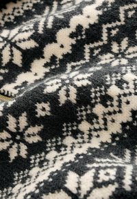 Tissu tricoté noir et crème avec un motif floral en flocon de neige, présentant une finition texturée et douce ainsi que des détails de fibres visibles.