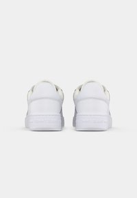 Baskets blanches avec tige en cuir lisse, bout arrondi, design minimaliste, discrète marque sur le talon et semelle en caoutchouc texturé.