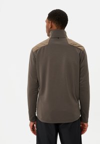 Pull en polaire marron avec un col élevé et des accents beige sur les épaules ; texture douce, manches longues et coupe décontractée.