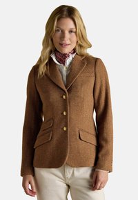 Blazer căptușit de culoare maro în model herringbone, cu croi ajustat, revere tăiate, butoane aurii și două buzunare frontale. Purtați peste o cămașă albă cu detalii imprimate.