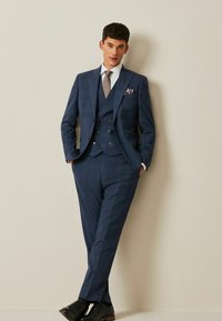 Navy checkered three-piece suit with a textured fabric, a white shirt, and a patterned tie. Completed with black shoes and a pocket square.