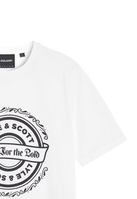 Camiseta de algodón blanca con un gráfico circular negro que muestra el texto "Lyle & Scott" y "For the Bold" en un estilo de pancarta. Mangas cortas.