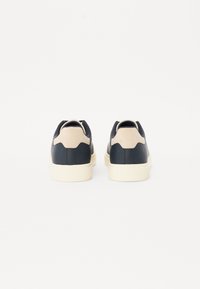 Baskets noires et beige avec une finition en cuir lisse, un dos texturé et de épaisses semelles en caoutchouc crème.