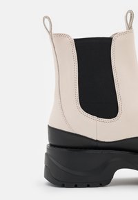Bottine en cuir beige et noir avec panneau latéral élastique noir, languettes en haut et épaisse semelle noire chunky.