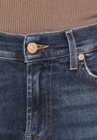 Jeans in denim blu scuro con chiusura a bottone in ottone, cuciture a contrasto e design a gamba dritta. Presentano un layout tipico a cinque tasche.
