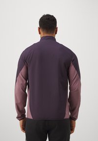 Dunkellila Sportjacke mit Stehkragen und kontrastierenden helllila Ärmeln. Glatte Textur, figurbetontes Design und elastische Bündchen.