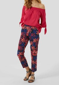 Rød off-shoulder top med bindesleeves, blomsterede marineblå bukser med pink og orange blomster, parret med strappy sandaler.