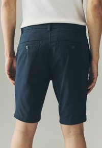 Mørkeblå bomulds shorts med slim fit, der har to baglommer med knapper og en glat tekstur, der går lige over knæene.