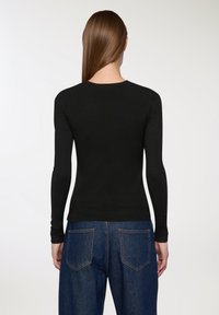 Czarny sweter z długimi rękawami o dopasowanym kroju i okrągłym dekolcie. Materiał wydaje się gładki, z prążkowanym wykończeniem u dołu i przy mankietach. Noszony z niebieskimi dżinsami.